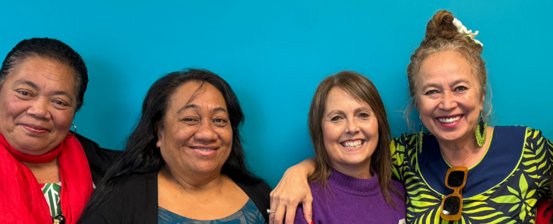 Four women standing together and smiling against a blue background.